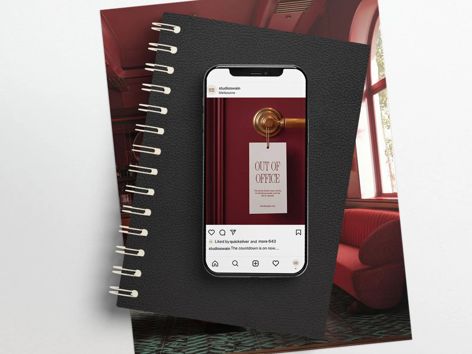 Black spiral-bound notebook with a smartphone displaying a coffee shop app on top, with a blurred interior background.