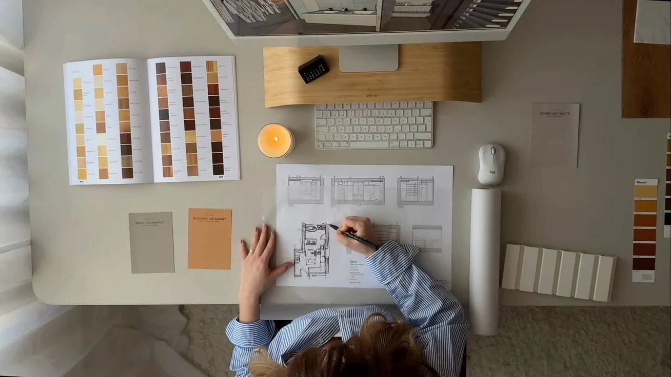 Person working at a desk with architectural plans, color swatches, and a lamp.